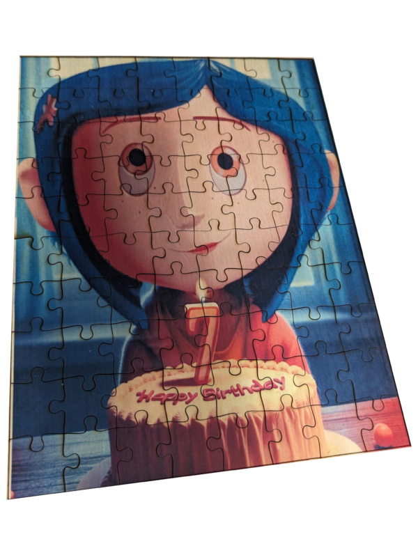 A wooden jigsaw puzzle depicting a cartoon of a girl with blue hair holding a birthday cake, completed and displayed on a textured surface.