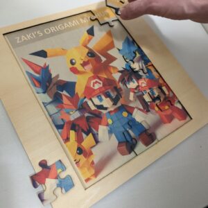 A wooden jigsaw puzzle featuring colorful origami animals, including a prominent Pikachu, being assembled on a white surface. A hand is placing the final piece.