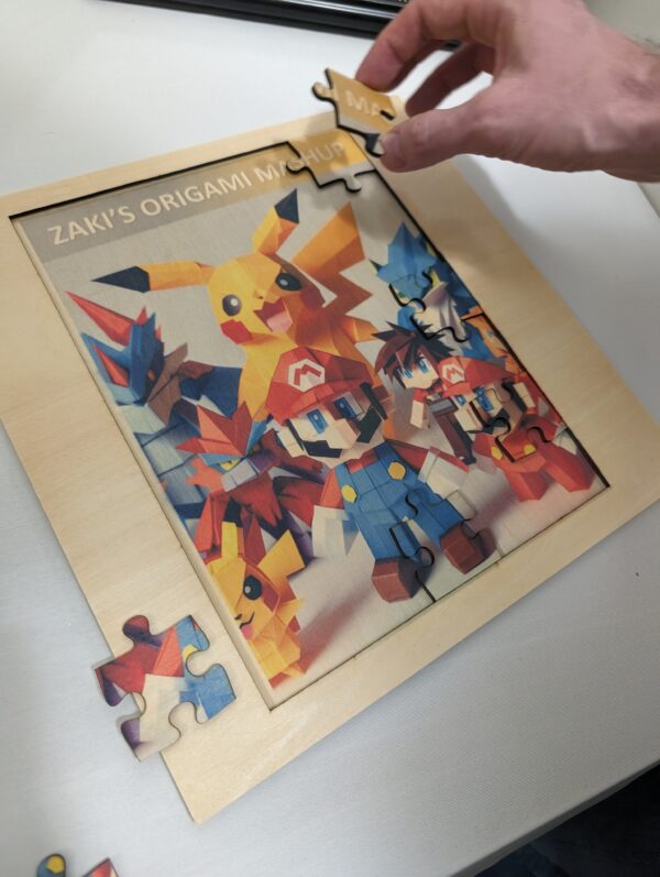 A wooden jigsaw puzzle featuring colorful origami animals, including a prominent Pikachu, being assembled on a white surface. A hand is placing the final piece.