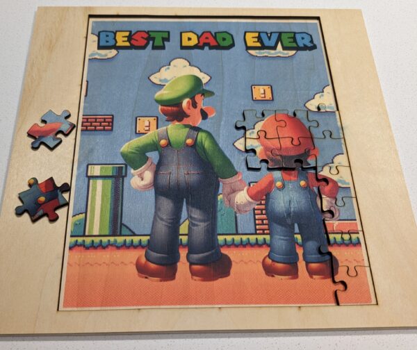 A jigsaw puzzle image of a father and child in iconic gaming attire, standing hand-in-hand against a vibrant game-themed backdrop, with ‘BEST DAD EVER’ written at the top.MARIO, Luigi