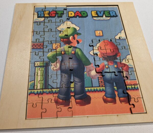 A jigsaw puzzle image of a father and child in iconic gaming attire, standing hand-in-hand against a vibrant game-themed backdrop, with ‘BEST DAD EVER’ written at the top.MARIO, Luigi