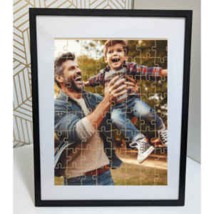 A framed puzzle depicting an adult lifting a child in the air, both faces obscured for privacy. The scene is set outdoors with a blurred natural background, suggesting a moment of joy and playfulness.These are custom Jigsaw puzzles. Perfect for gifts, birthdays, mothers day, christrmas, teachers, thanksgiving, decorations. With personal photos.